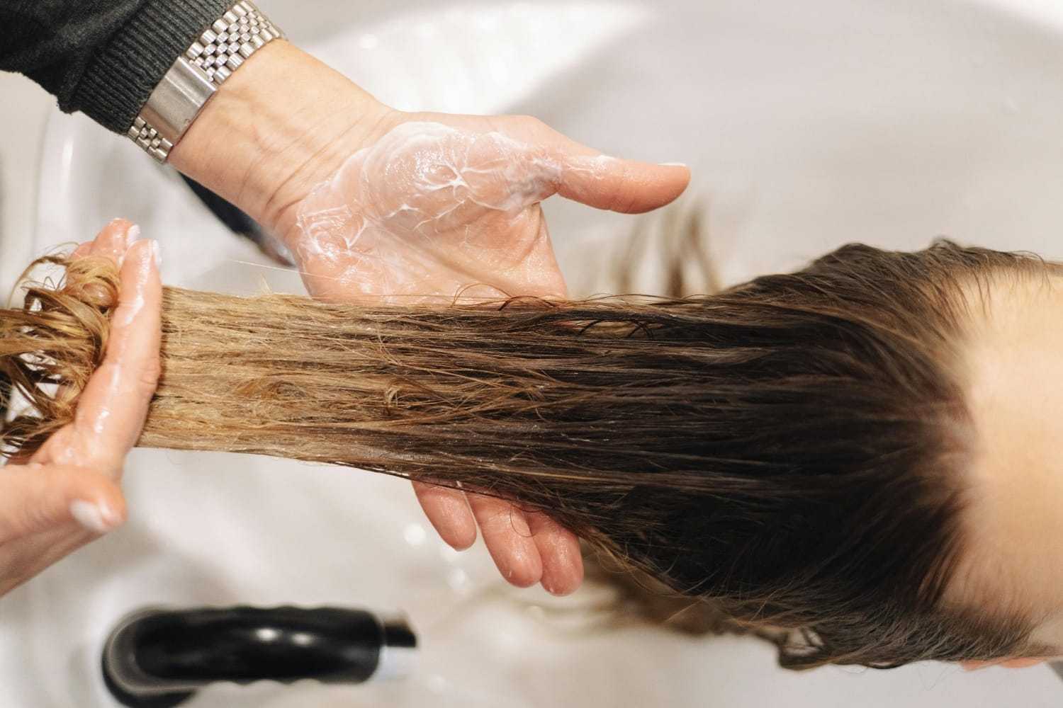 Hands applying shampoo to wet hair in a salon sink.