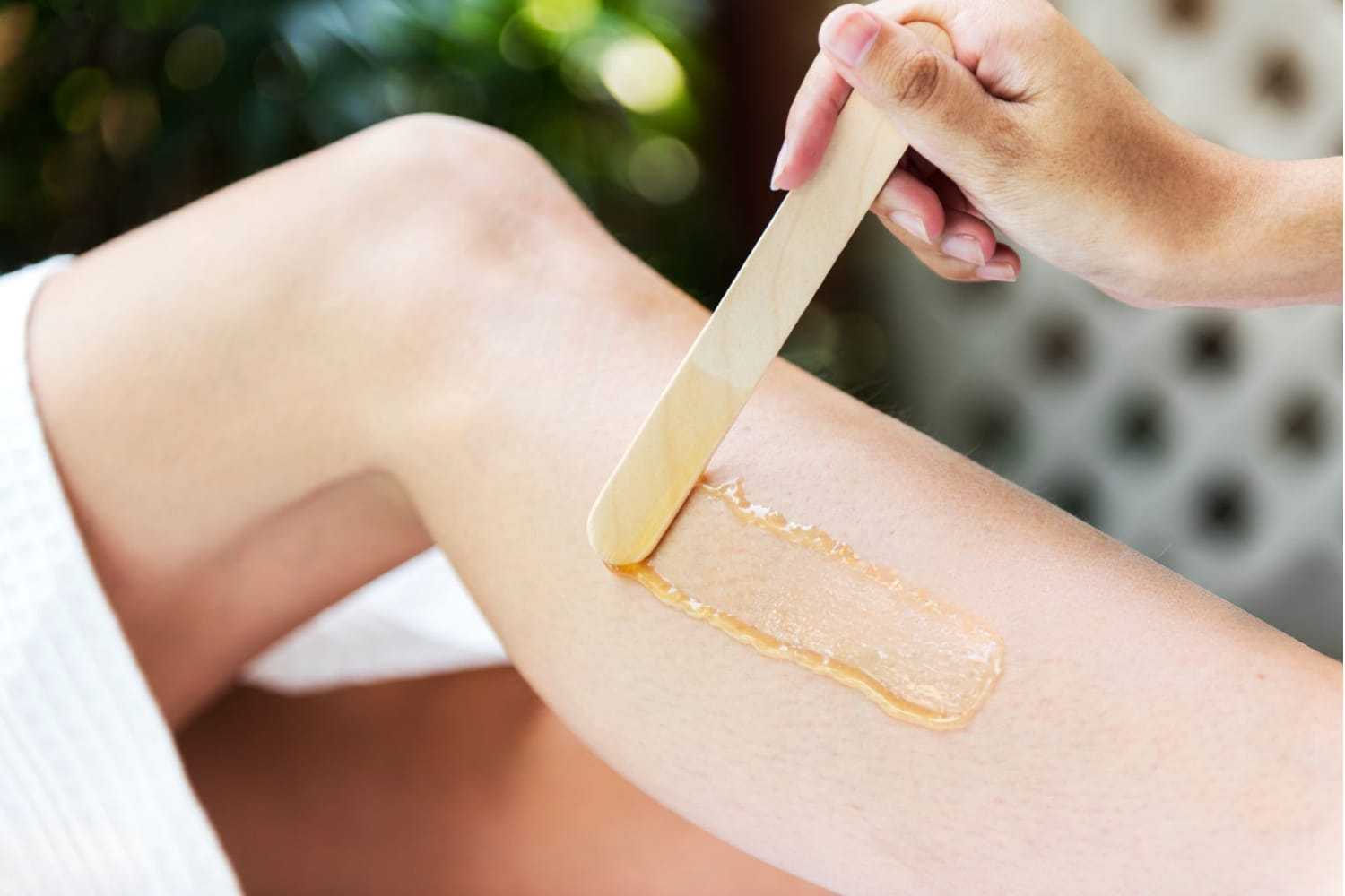 Leg being waxed with a wooden spatula applying wax in a spa setting.
