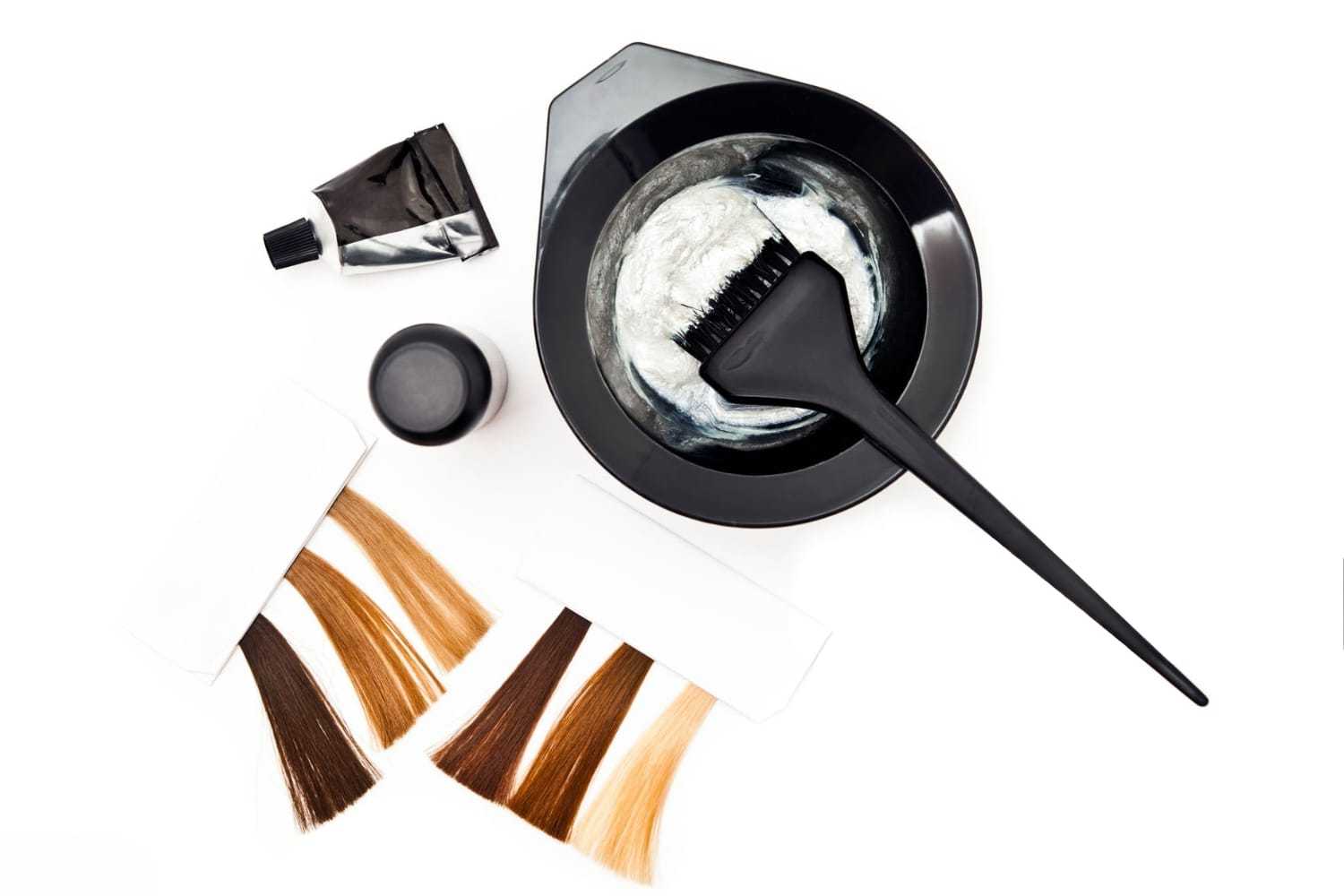 Hair dye tools and color samples with brush in mixing bowl.