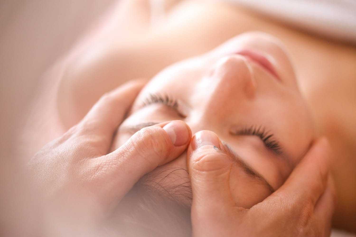 Massage therapist applying gentle pressure to forehead of a relaxed person in a spa setting.